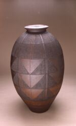 Tall oval urn with finely scored design of interlocking triangles. Bronze/black. Height 75cm/30”.